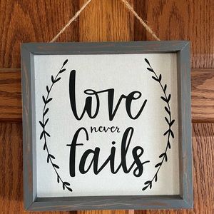 “Love Never Fails” decor sign